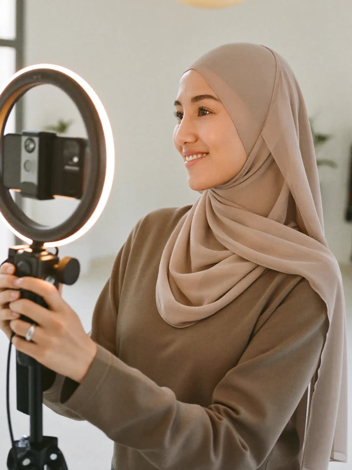 صانعة محتوى عربية ترتدي الحجاب وتصوّر مقطعًا أمام إضاءة دائرية وهي تبتسم